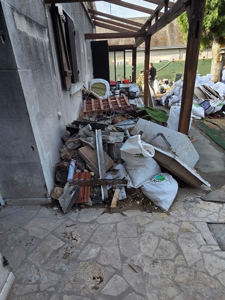 Terrasse sous pergola encombrée de gravats, de tôles et de sacs de déchets à évacuer