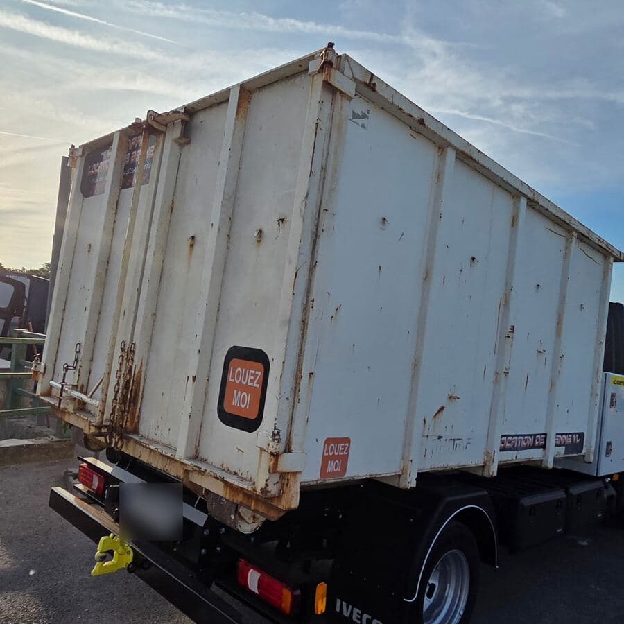 Camion vu de l’arrière, chargé d’une benne blanche portant l’autocollant « Louez-moi », plaque floutée